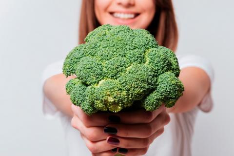 Mujer enseñando un vegetal crucífero, brócoli