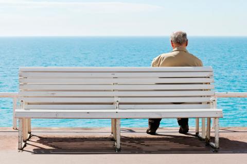 Anciano solo sentado en un banco frente al mar