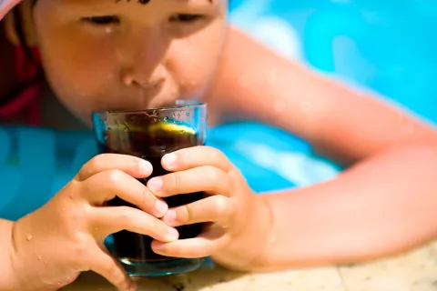 Niño toma un refresco mientras se baña en la piscina