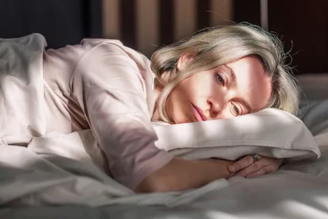 Mujer con cabello blanco intenta dormir con cara de cansada sobre la amohada