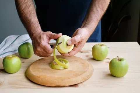 Hombre pelando la piel de una manzana verde