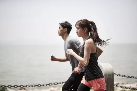 Joven pareja asiática corriendo al aire libre junto al mar