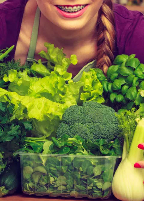 Mujer joven sosteniendo entre sus brazos un monto de vegetales distintos