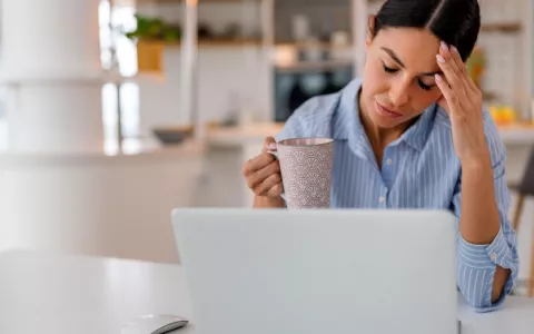 A una mujer con una taza de café le cuesta prestar atención a la pantalla de su ordenador Mujer con aspecto cansado sostiene una taza de café frente a su portátil
