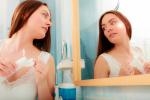 Una joven se limpia el rostro con agua micelar frente al espejo