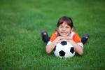 Una niña tumbada en la hierba abraza un balón de fútbol sonriendo