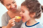 Beneficios y riesgos del queso para la salud Madre da de comer queso a su hija pequeña