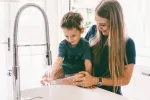 Higiene en la cocina y defensas en el cáncer infantil Madre e hijo lavándose las manos en la cocina