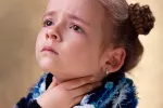 Factores que influyen en la voz de los niños Una niña se toca la garganta con gesto de dolor
