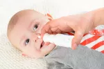 Productos para la higiene nasal y oral del bebé Un padre aplica suero fisiológico en la nariz de su bebé