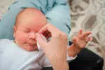 Productos para la limpieza de los ojos del bebé Un padre limpia los ojos de su bebé con unos algodones