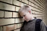 Niño triste con la cabeza apoyada en una pared