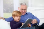 Un abuelo consulta una tablet con su nieto Los cambios de hogar dificultan la atención médica de los mayores