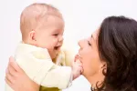 El amor materno favorece el desarrollo del cerebro del niño Una madre levanta a su bebé en brazos, sonriéndole mientras él le toca la cara