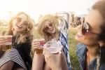 Cada vez más adolescentes se dan atracones de alcohol Tres chicas muy sonrientes en un parque sostienen vasos de cerveza