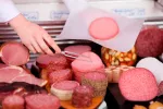 Comer carne procesada aumenta el riesgo de cáncer Charcutero prepara un pedido en un mostrador repleto de embutidos