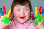 Niña con Síndrome de Down con las manos pintadas y feliz
