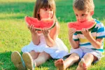 Los niños que siguen una dieta saludable tienen mejor autoestima Niños sentados comiendo sandía en el campo