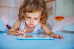 Los dispositivos con pantalla perjudican el sueño infantil Una niña pequeña juega con una tablet en su dormitorio