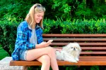 Una joven consulta en su móvil dónde puede ir con su perrito, tumbado junto a ella