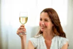 Tomar vino blanco incrementa el riesgo de rosácea en las mujeres Mujer con rosácea levanta una copa de vino blanco