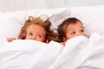 Miedos y fobias infantiles Niña y niño asustados en la cama tapándose la boca con la sábana