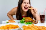Mujer joven cenando multitud de alimentos grasos