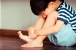 NIño sentado en el suelo de la habitación mirando al suelo