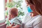 Los bebés contagian más el COVID-19 en el hogar que los adolescentes Mujer con una mascarilla cuidando de su bebé