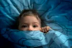 Miedo a la oscuridad en los niños NIño austado metido entre las sábanas de la cama