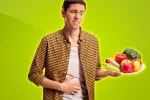 Dieta con verduras mejora la microbiota y causa más gases en hombres Joven mirando un plato de verduras y con dolor de estómago