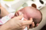 Madre aplicando pomada protectora para evitar una conjuntivitis en su bebé