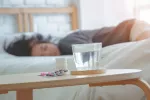 Mujer dormida junto a un vaso de agua y pastillas