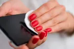Descubren altos niveles de alérgenos en los móviles y cómo eliminarlos Mujer limpiando la pantalla de su móvil