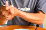 Anciano con párkinson sujetándose la mano para comer