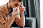 Hombre joven enfermo por coronavirus sonándose la nariz con un pañuelo