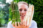 Una mujer sosteniendo dos manojos de espárragos blancos y verdes