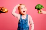 Lo que comemos de niños influye en nuestras preferencias alimentarias Niña intentando elegir entre una hamburguesa o brócoli.