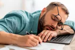 Vinculan la fatiga crónica a alteraciones en el microbioma intestinal Hombre dormido sobre el escritorio de trabajo