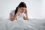 Mujer joven se incorpora en la cama con gesto de dolor