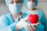 El COVID aumenta un 55% el riesgo de sufrir eventos cardiovasculares Una doctora con mascarilla sosteniendo un corazón de plástico
