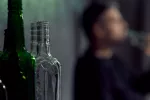 Identifican causas de la conducta autodestructiva y las adicciones Persona junto a un montón de botellas de alcohol vacías