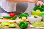 Mujer embarazada preparando una ensalada con verduras y aceite de oliva