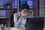Las gafas con filtro de luz azul no reducen la fatiga visual Mujer joven se frota los ojos sujetando las gafas frente a un portátil