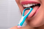 Cómo limpiar tu lengua y qué problemas la afectan Mujer limpiando su lengua con un rascador