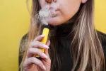 Vapear inmoviliza las células de defensa del cuerpo Chica rubia vapeando con su cigarrillo electrónico amarillo