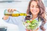 Seguir la dieta mediterránea mejora la salud del hígado y la microbiota Mujer echando aceite de oliva a una ensalada
