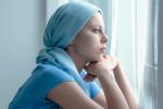 Mujer enferma de cáncer con la mirada perdida frente a una ventana 