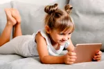 Niña pequeña tumbada en el sofá jugando con la tablet