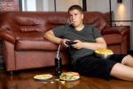 NIño obeso comiendo 'fast food' en el sofá de su casa y jugando a la videoconsola